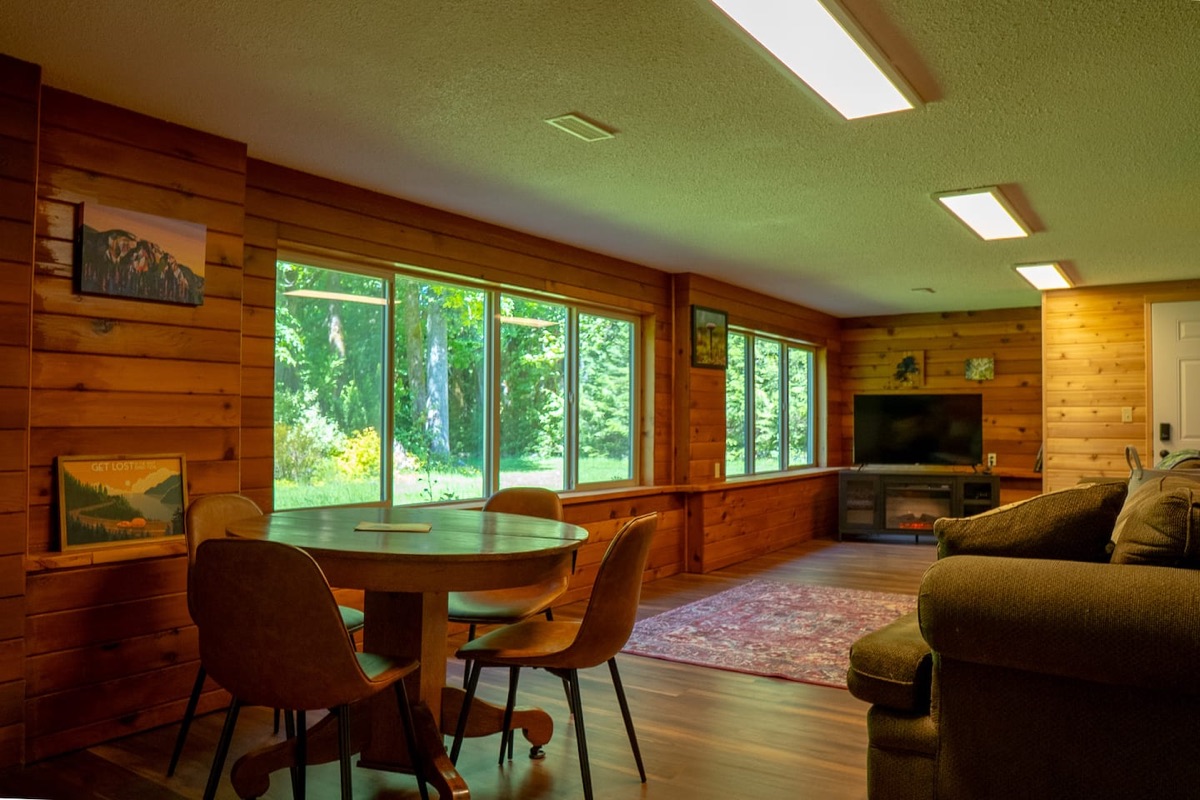 Cedar-panelled living room with dining area, fireplace, and forest views