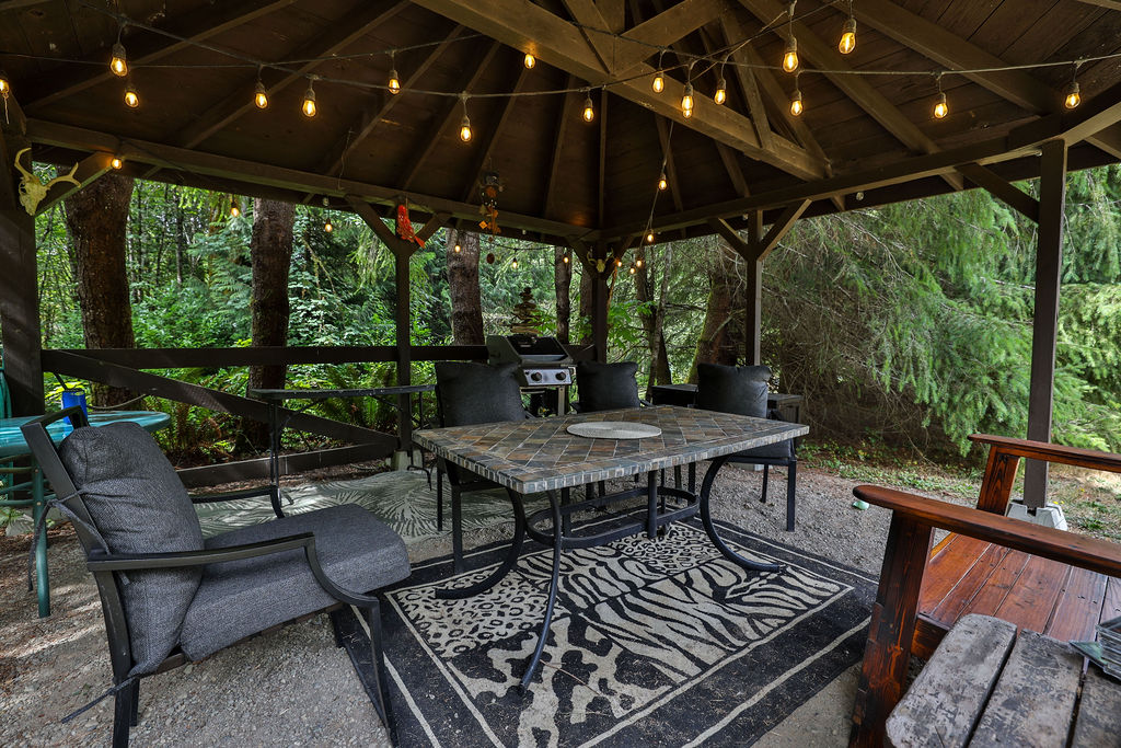 Covered gazebo with string lights, dining table, and BBQ